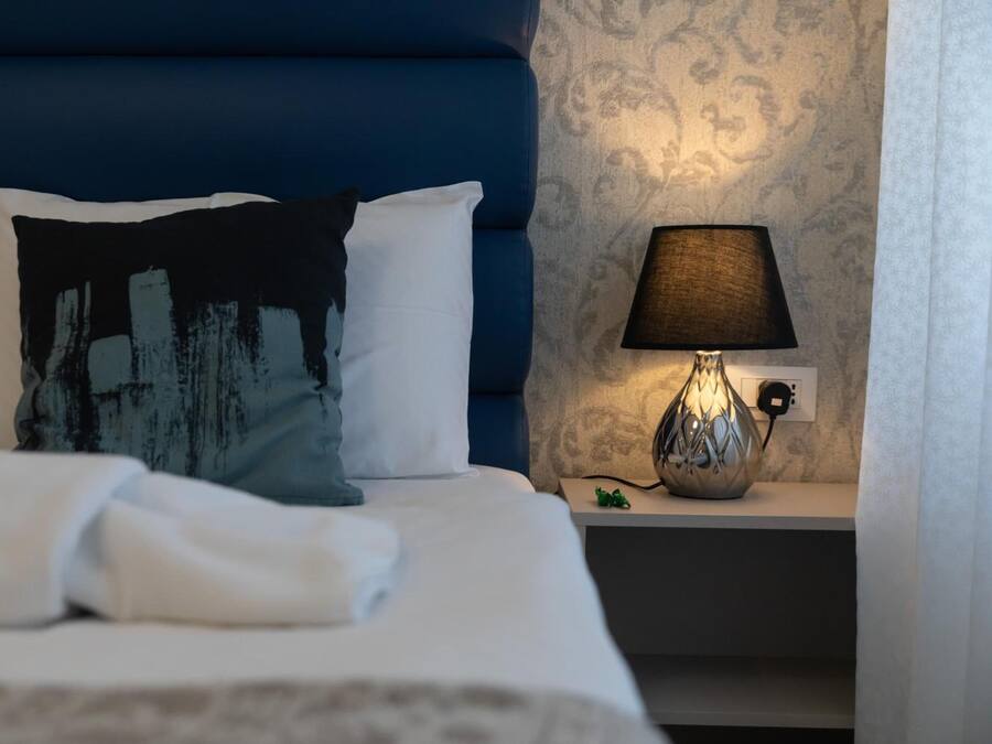 A neatly made bed with white linens, a blue headboard, and a decorative pillow. There is a bedside lamp on a nightstand beside the bed.