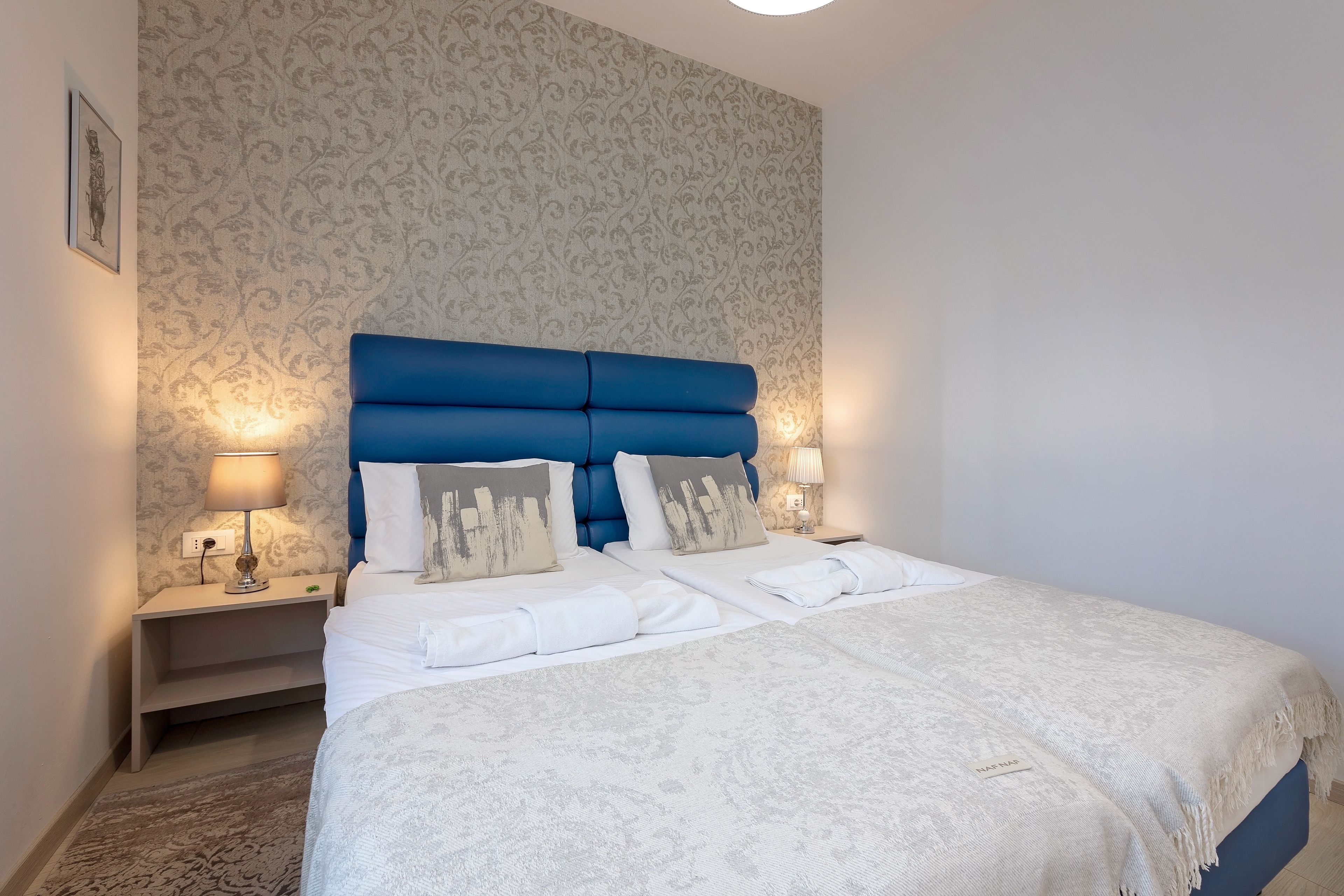 Una cama bien hecha con un cabecero azul, ropa de cama blanca y una pared con diseño.