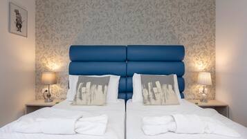 A double bed with a blue headboard, two bedside tables with lamps, and a patterned wallpaper.
