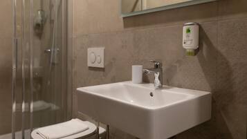 Une salle de bain avec un lavabo blanc, une cabine de douche en verre et des toilettes.