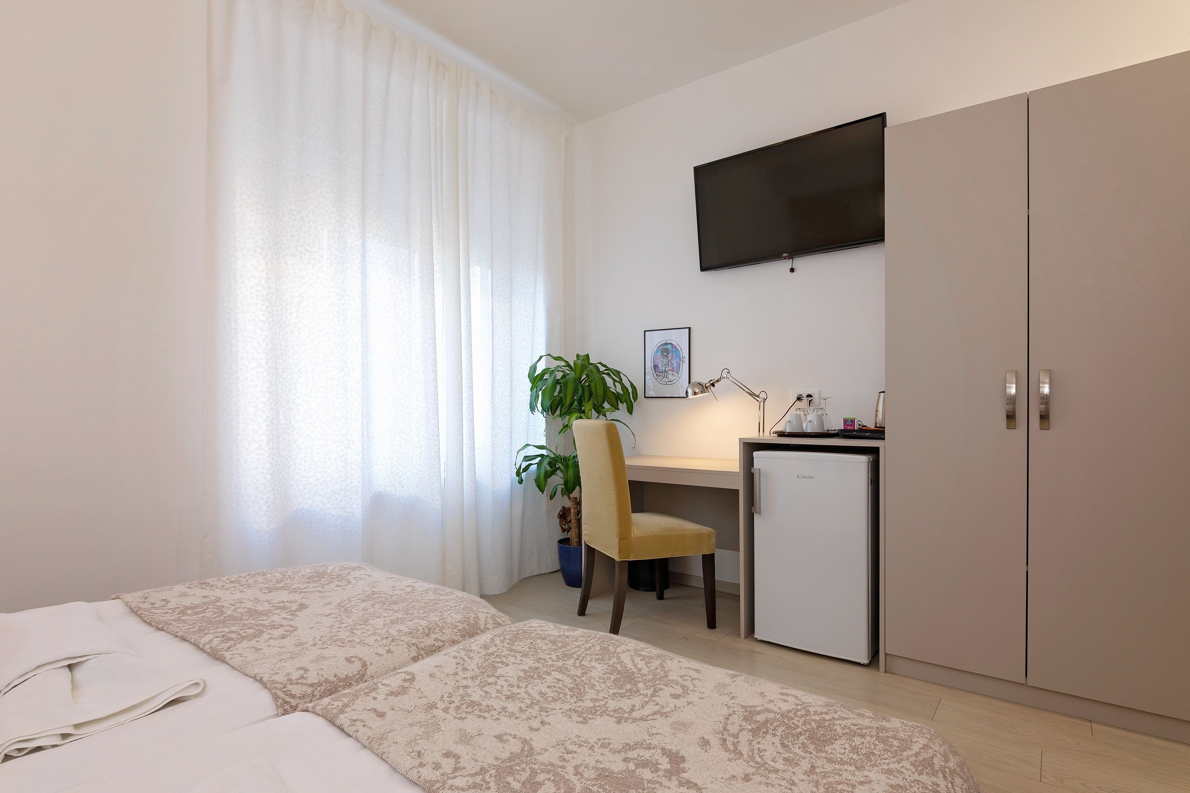 A hotel room with a bed, a desk, a chair, a television, and a wardrobe.