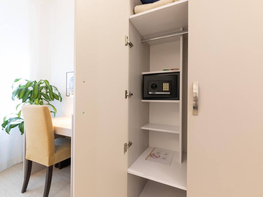 A room with a desk, a chair, a potted plant, and a white cabinet with a safe.