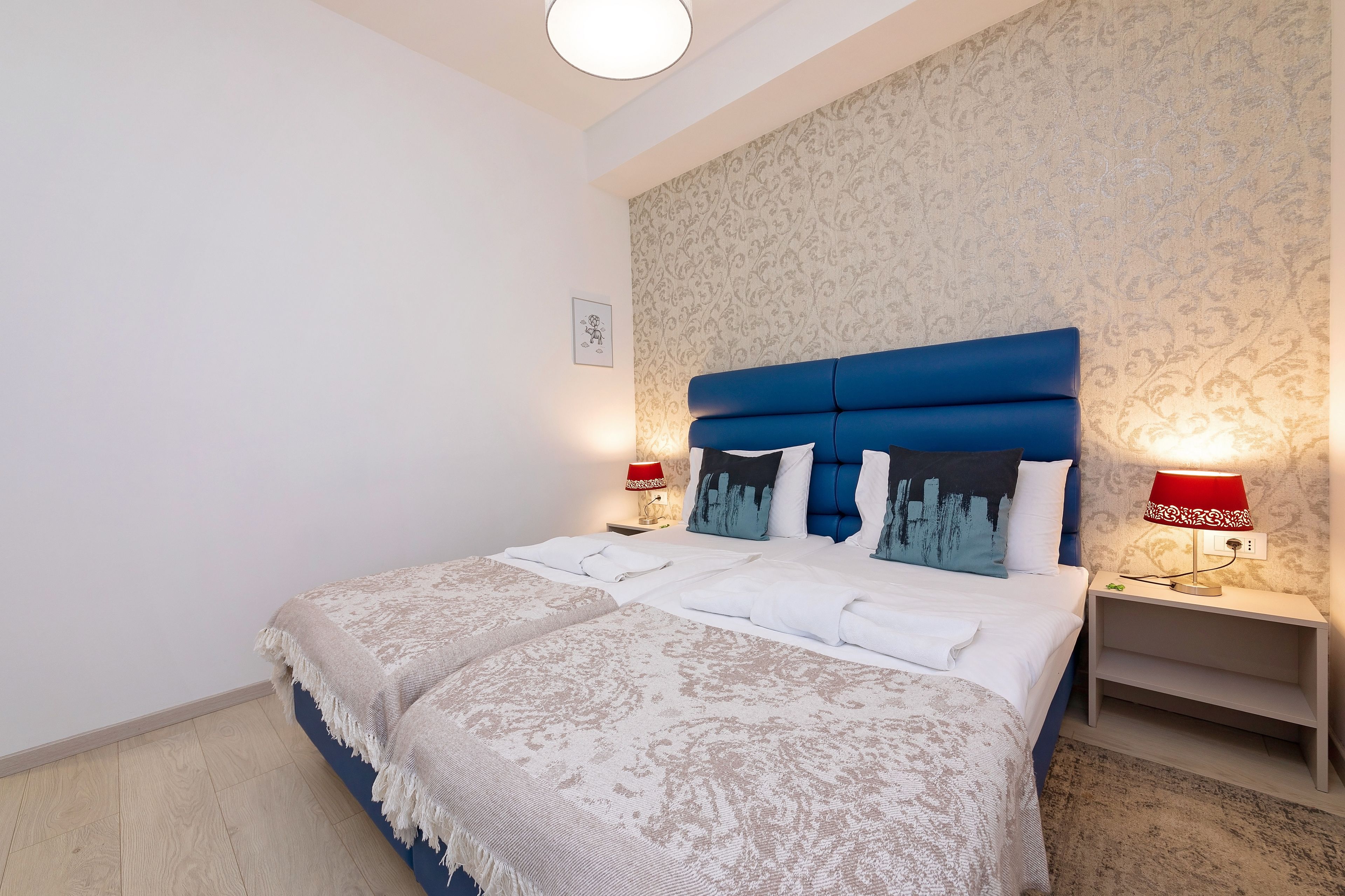 A neatly made bed with a blue headboard, two bedside lamps, and a patterned wall.