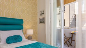 Habitación de hotel con cama, mesita de noche, lámpara y vistas al balcón exterior.