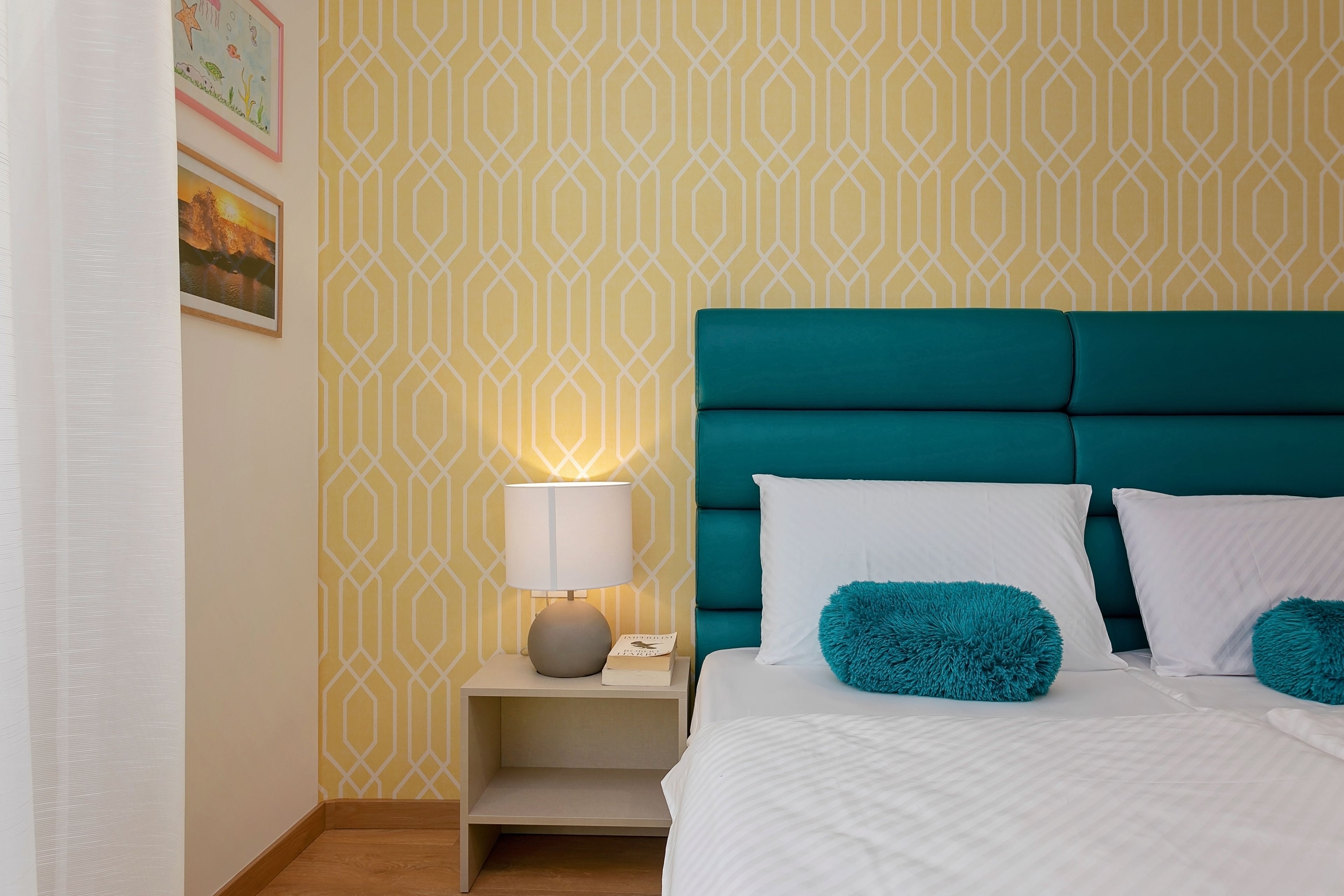 Un dormitorio ordenado con un cabecero color turquesa, ropa de cama blanca y almohadones turquesa.
