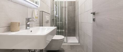 Un baño moderno con lavamanos, inodoro y cabina de ducha de vidrio.