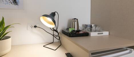 Un espacio de trabajo moderno con una lámpara de escritorio, una planta en maceta, un control remoto y una cafetera.