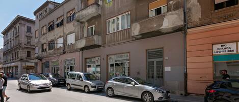 A street with parked cars and a building with a sign for 'BIG BRANDS LOW PRICES'.