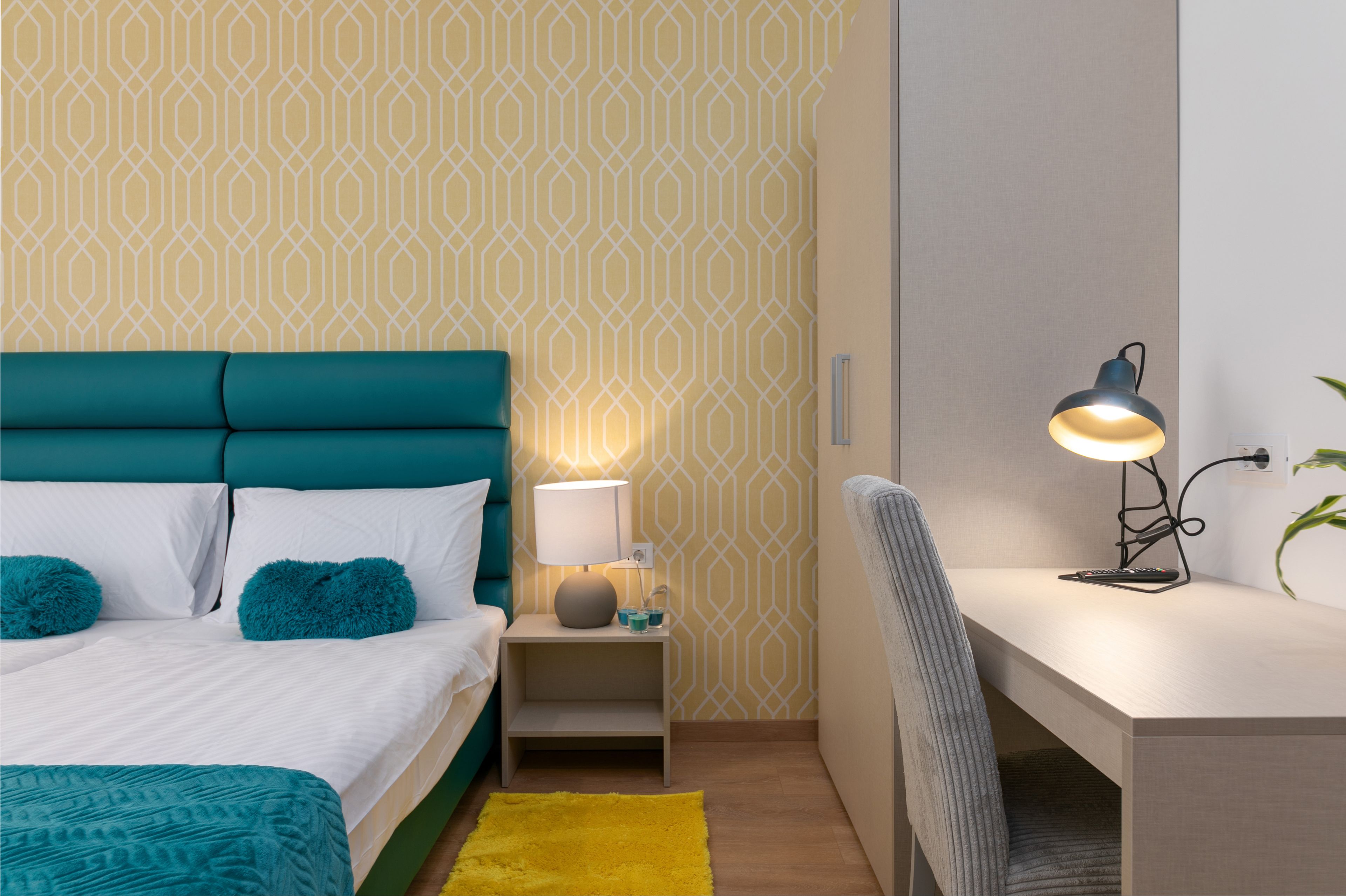Una camera da letto ordinata con un letto, un comodino, una lampada e una scrivania con una sedia.