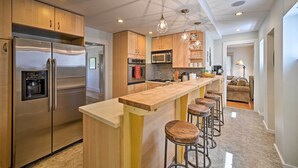 Una cocina moderna con refrigerador de acero inoxidable, armarios de madera, una isla central con taburetes e iluminación colgante.