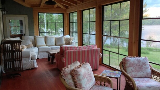 A cozy room with a wooden ceiling, large windows, wicker furniture, and a view of the outdoors.