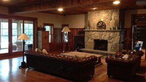 A spacious living room with a stone fireplace, leather sofas, and a wooden ceiling.