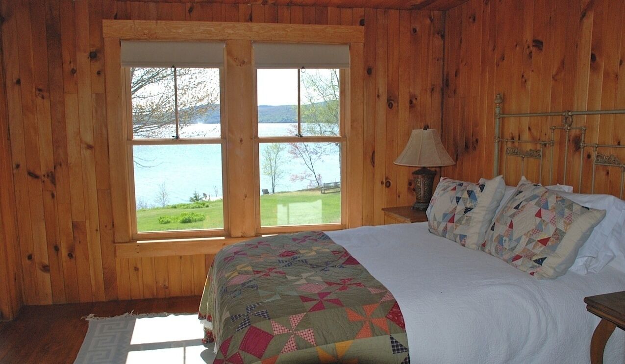 Un dormitorio de cabaña de madera con una cama grande, una mesita de noche y una ventana con vistas a un lago.