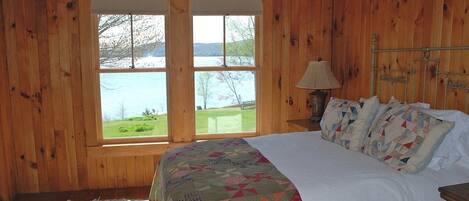 Un dormitorio de cabaña de madera con una cama grande, una mesita de noche y una ventana con vistas a un lago.