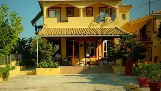 Un bâtiment à deux étages, doté d’une façade jaune, d’un toit en tuiles et d’antennes paraboliques sur le toit.