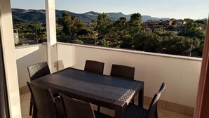 A covered outdoor patio with a table and chairs, offering a view of a hilly landscape with buildings in the distance. - THREE-ROOM APARTMENT WITH SOLARIUM AND POOL (Viddalba)