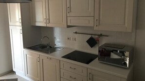A kitchen with white cabinets, a black countertop, a sink, a toaster, and a hanging pot rack. - THREE-ROOM APARTMENT WITH SOLARIUM AND POOL (Viddalba)