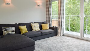 Ein modernes Wohnzimmer mit einem Ecksofa, zwei Wandleuchten und einer großen Glasschiebetür, die auf einen Balkon führt.