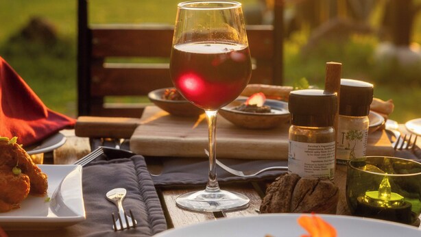 Una mesa dispuesta para una comida, con una copa de vino tinto, platos de comida y una vela.