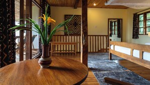 Una mesa de madera con un florero de flores amarillas, un banco de madera y una pared con diseño en una habitación con vigas de madera y ventanas amplias.