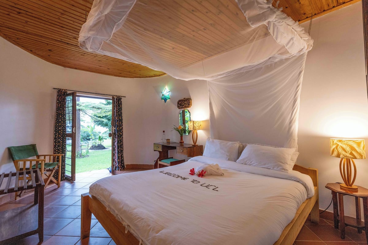 Quarto com cama de dossel, escrivaninha, cadeira e vista para o exterior.