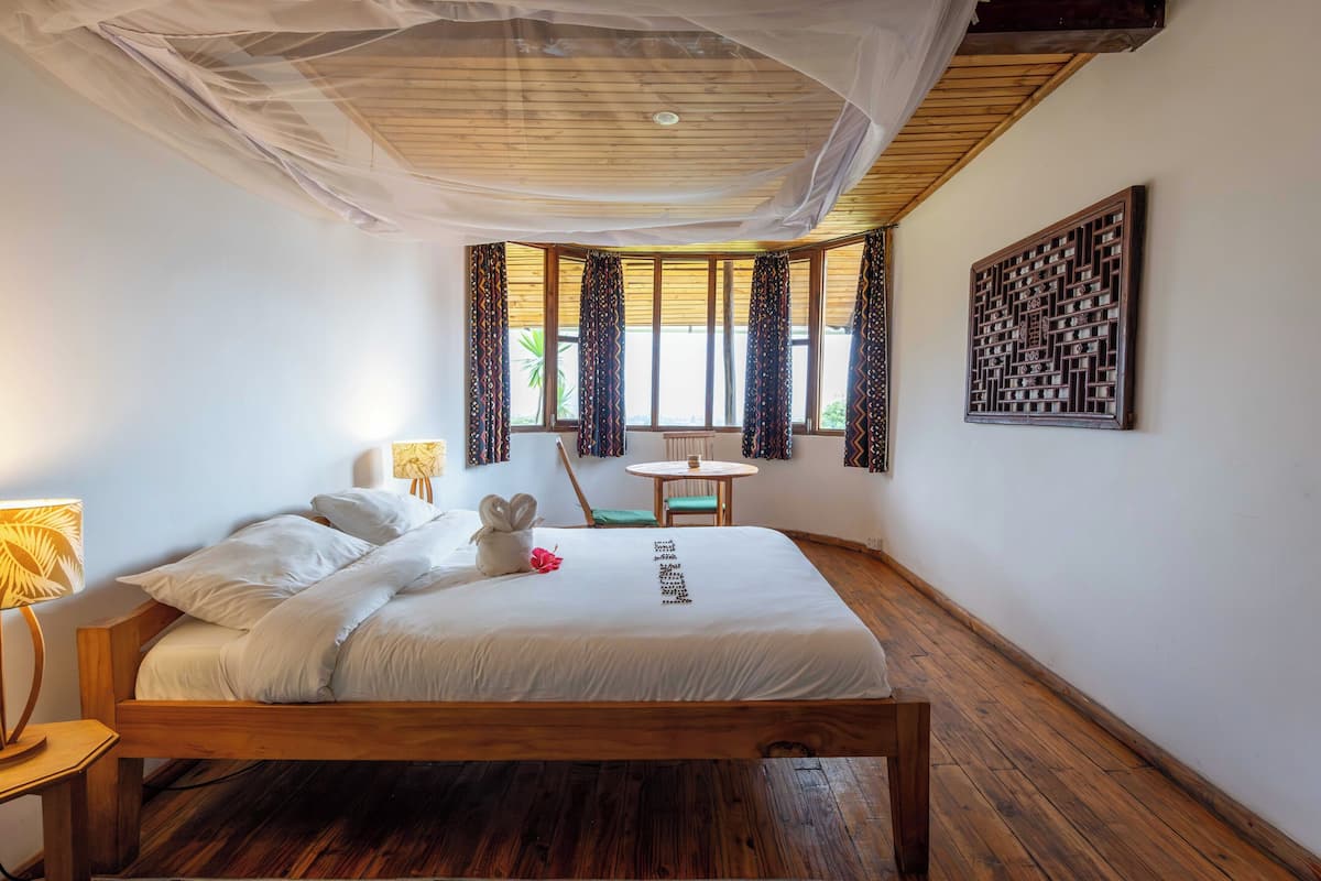 Quarto com cama de madeira, uma mesa redonda pequena, uma cadeira e um objeto decorativo na parede.