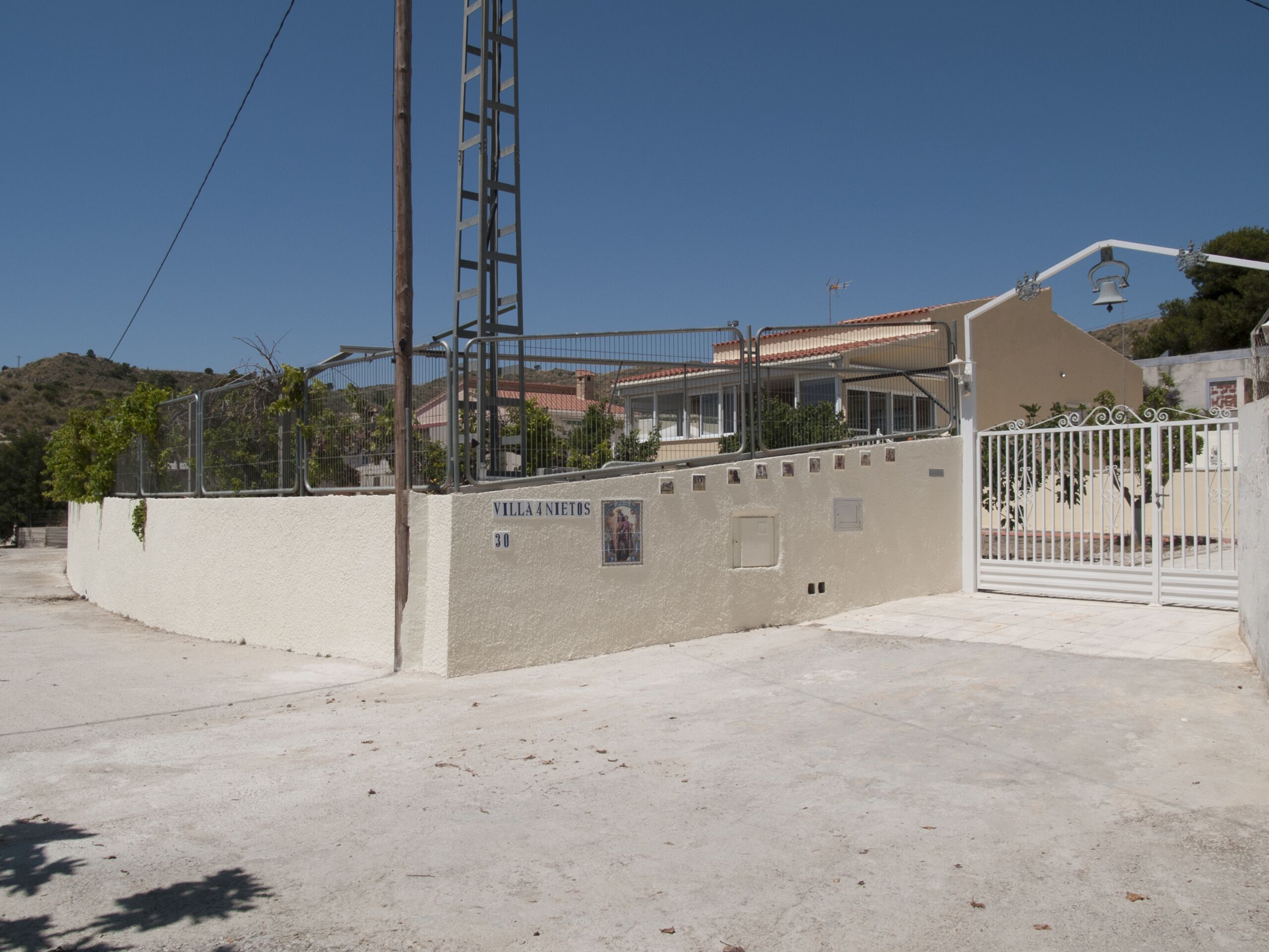 A gated residential area with a concrete wall, a metal gate, and a building with a red roof.