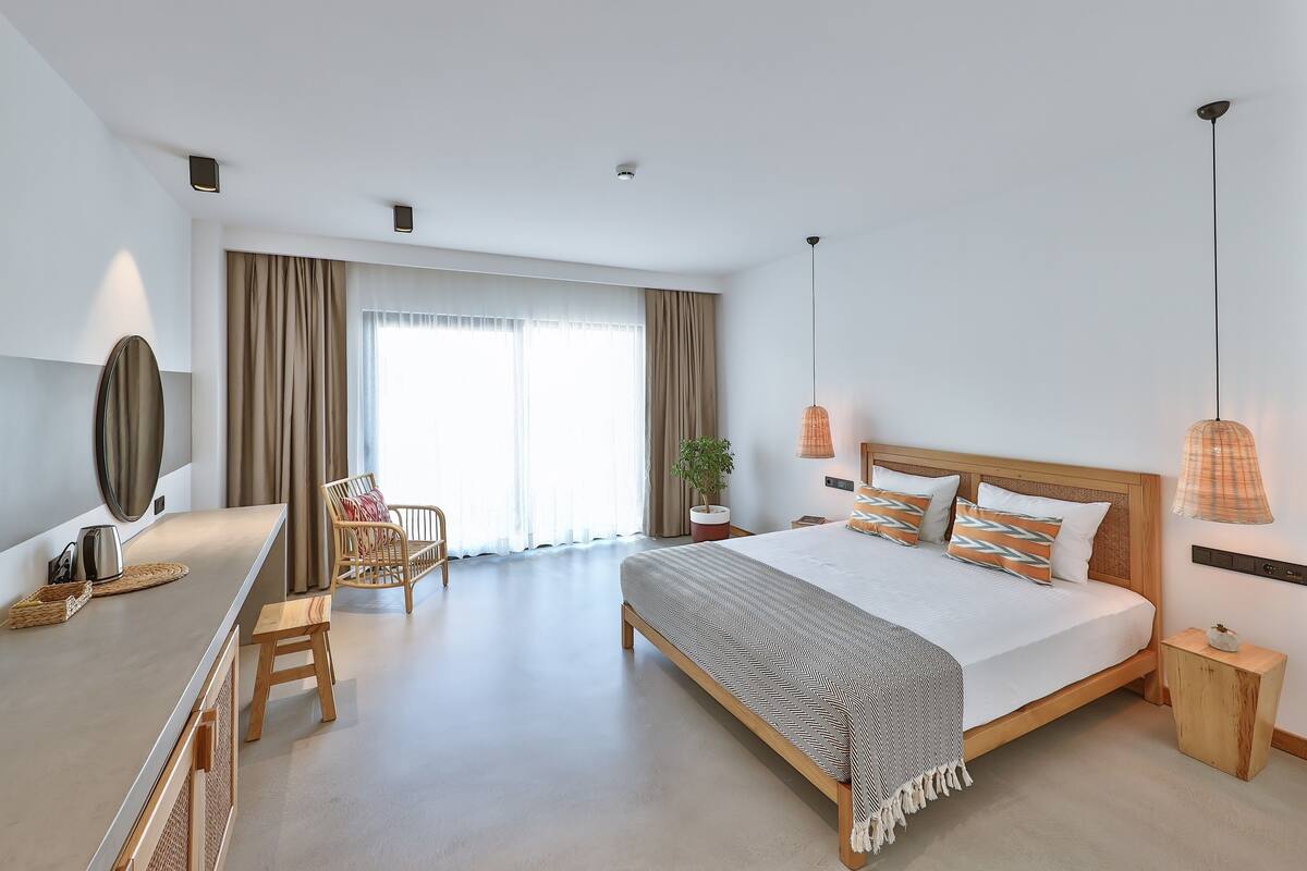 Una habitación de hotel moderna con una cama grande, un escritorio, una silla y un ventanal con cortinas.