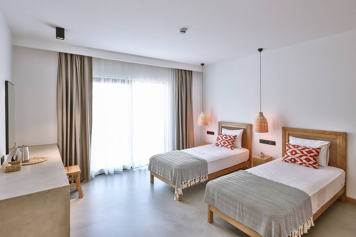 Una habitación de hotel moderna con dos camas, un escritorio y un ventanal grande con cortinas.