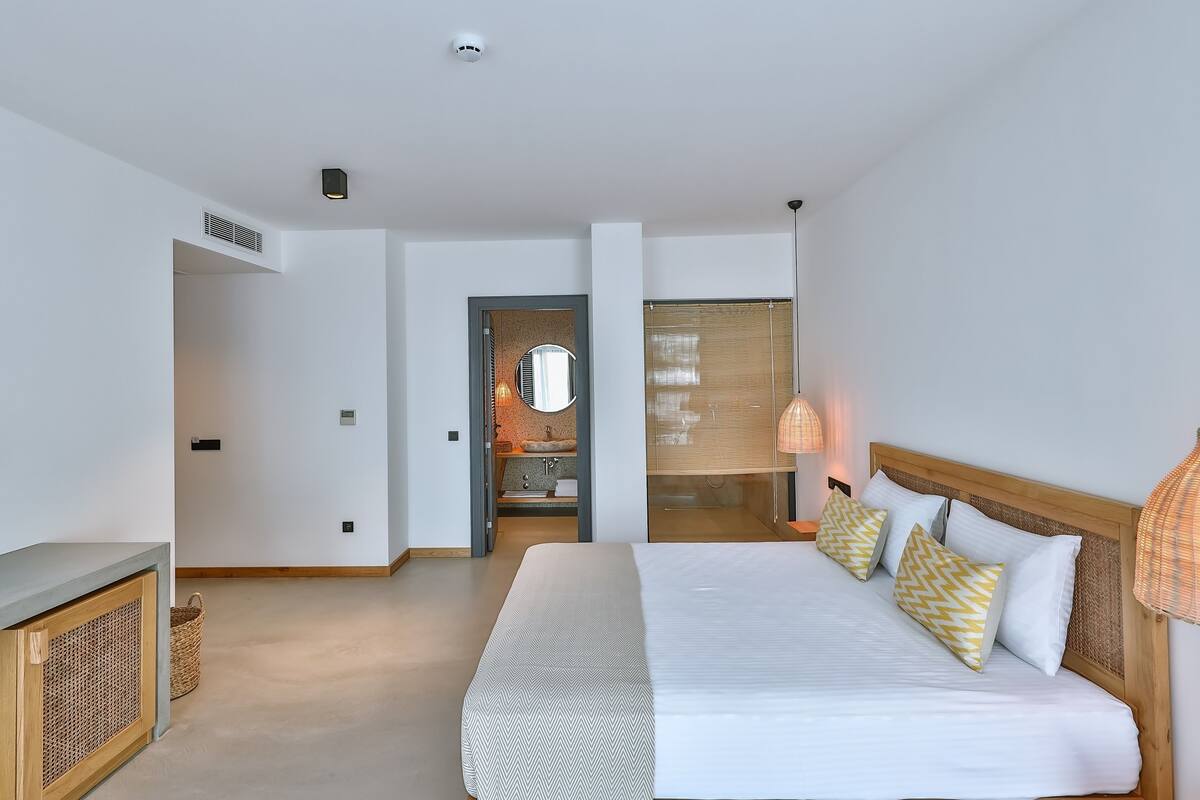 Una habitación de hotel moderna con una cama grande, un cabecero de madera, una lámpara de noche y vistas al baño.