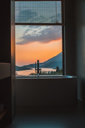 A room with a large window overlooking a sunset over a body of water and mountains. - Carruba Boutique Hotel (Kas)