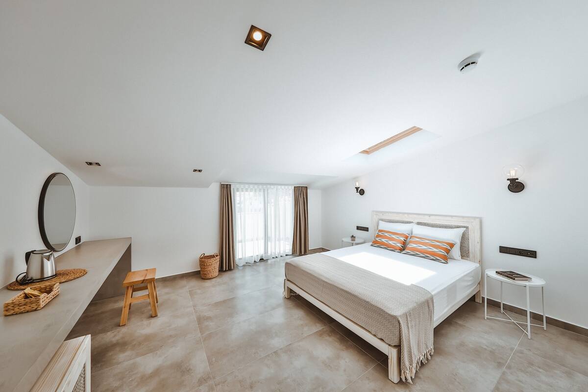Un dormitorio moderno con una cama grande, una mesita de noche, un taburete pequeño, un espejo y una lámpara en el techo.