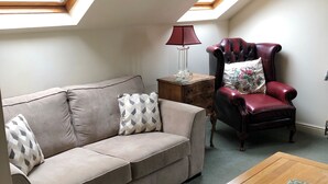 Un salon chaleureux avec un canapé, une table basse en bois, un fauteuil en cuir rouge et une table d’appoint avec une lampe.