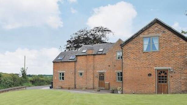 Une maison à deux étages, construite en briques, avec une grande pelouse devant.