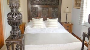 Une chambre à coucher avec un grand lit, une tête de lit en bois ornée de motifs complexes, une grande lampe décorative et une table de chevet avec une lampe.