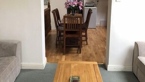 Un coin repas avec une table et des chaises en bois, une cuisine en arrière-plan et un canapé gris au premier plan.