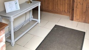 Un escalier avec des rampes en bois, une console blanche surmontée d’une lampe et d’un certificat, et un tableau encadré accroché au mur.