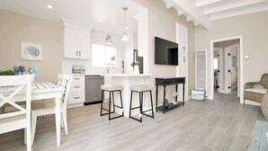 Un grand espace de vie comprenant une cuisine, une table à manger avec des chaises, un coin bar avec des tabourets et un téléviseur fixé au mur.