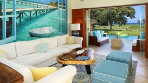 A spacious living room with a white sofa, a wooden coffee table, and a view of a pool and garden through large windows.
