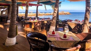 An outdoor dining area with tables and chairs, palm trees, and a view of the beach and ocean.