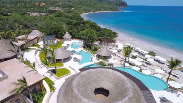 A resort with multiple swimming pools, a beach, and thatched-roof structures.