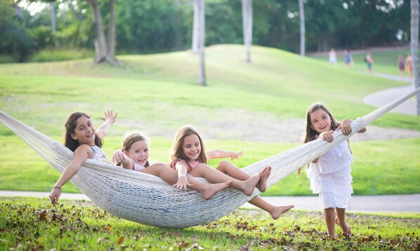 A hammock with four children in a grassy outdoor area.