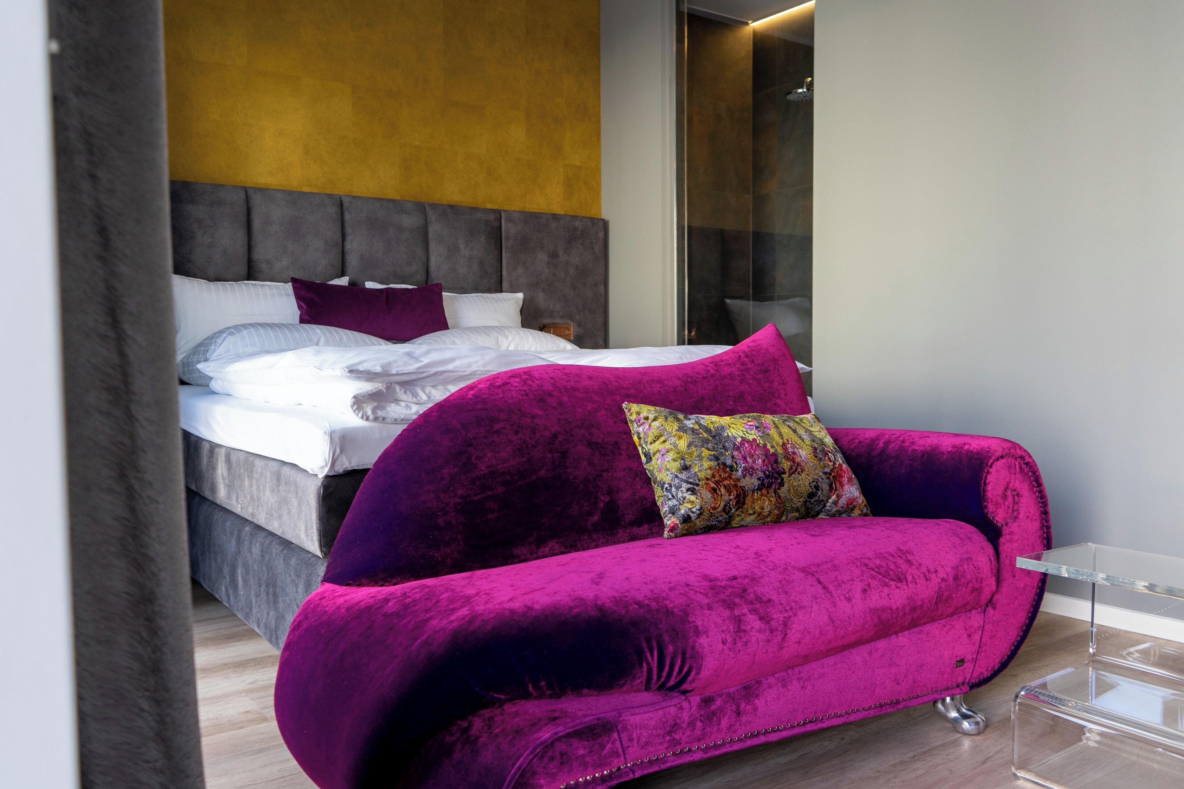 Une chambre à coucher moderne avec un lit, un canapé rose vif et une table basse en verre transparent.
