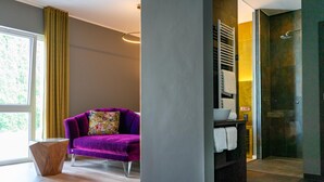 Un baño moderno con cabina de ducha de vidrio, un sofá púrpura con un cojín floral y una mesita de madera.