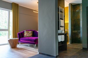 Un baño moderno con cabina de ducha de vidrio, un sofá púrpura con un cojín floral y una mesita de madera.