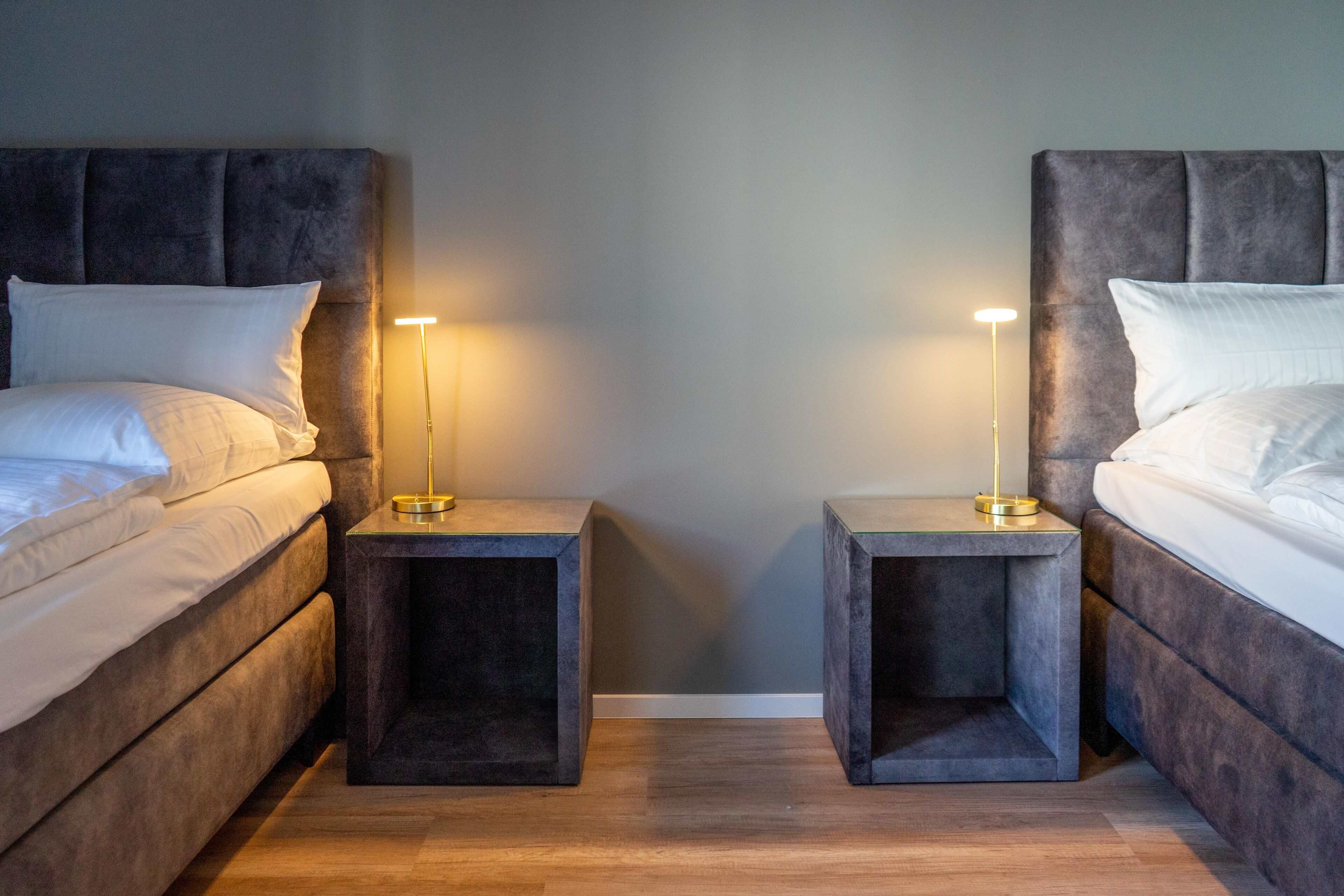 Een slaapkamer met twee bedden, elk met hoofdeinde, en nachtkastjes met lampen ernaast.