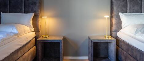 Een slaapkamer met twee bedden, elk met hoofdeinde, en nachtkastjes met lampen ernaast.