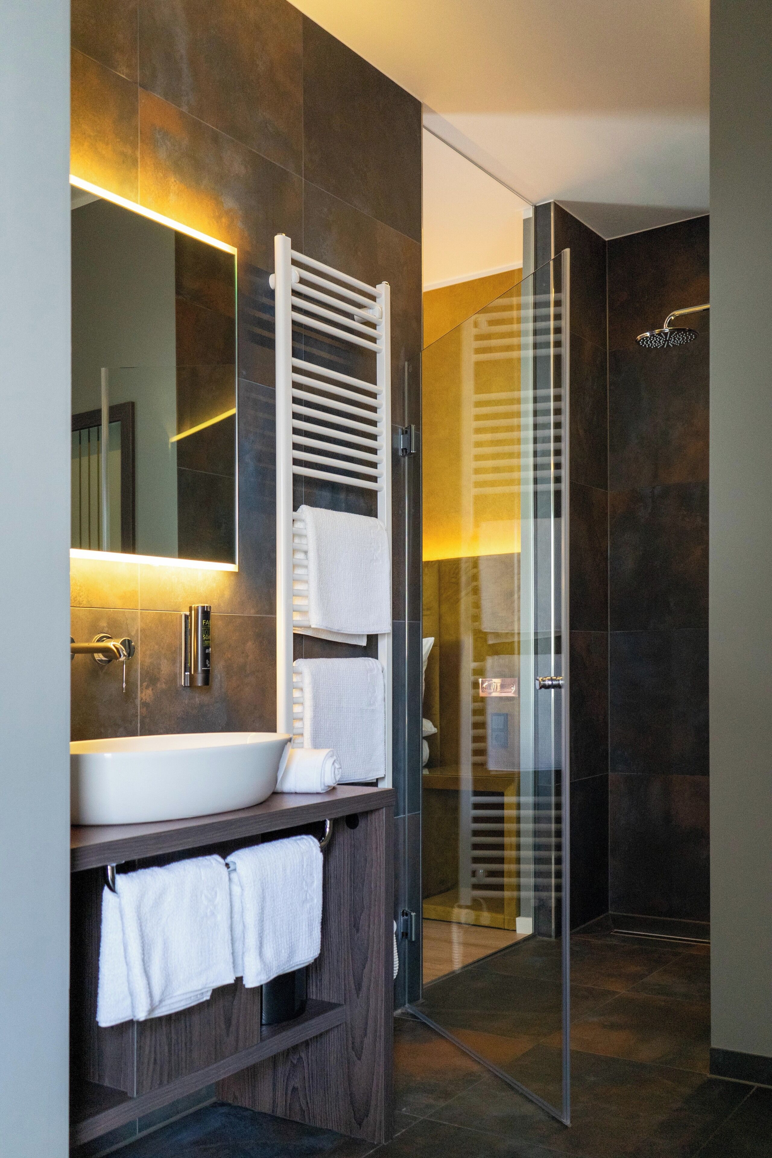 A modern bathroom with a large mirror, a white sink, a towel rack, and a glass shower enclosure.