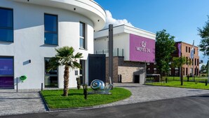 Un hotel moderno con una fachada curva, un llamativo letrero púrpura y una escultura espiral decorativa en la zona de entrada.