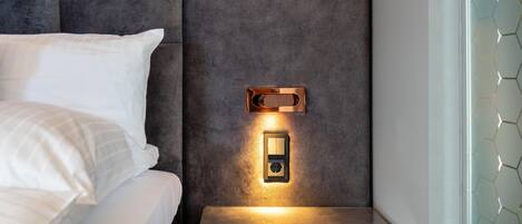 A modern hotel room with a bed, a glass side table, and a wall-mounted light fixture.